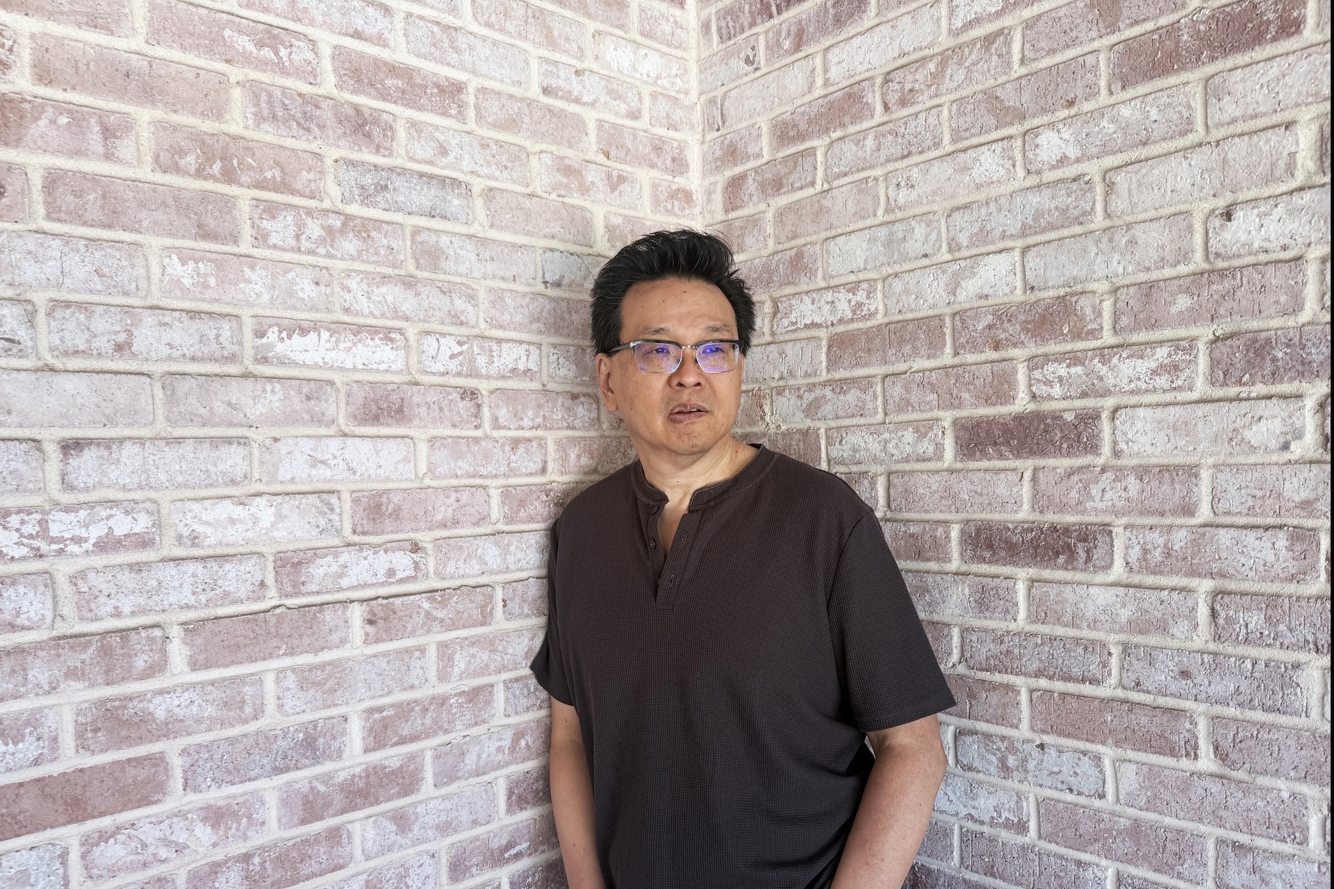 Andy Koh, Dallas-based singer-songwriter and pediatric oncologist, standing against a whitewashed brick wall, photo credit Andy Koh