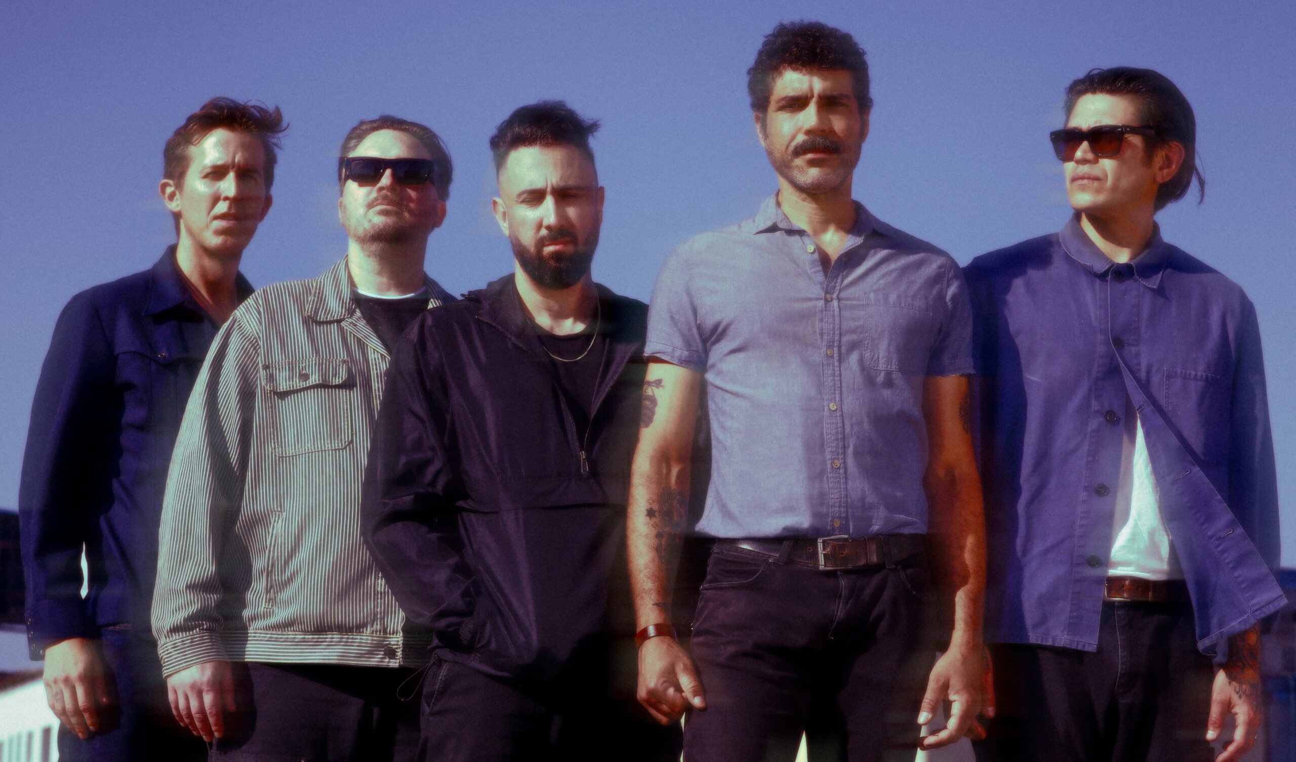 Drag Talk, the Los Angeles shoegaze and indie rock band, standing together outdoors against a blue sky, photo by Yiyi Wan