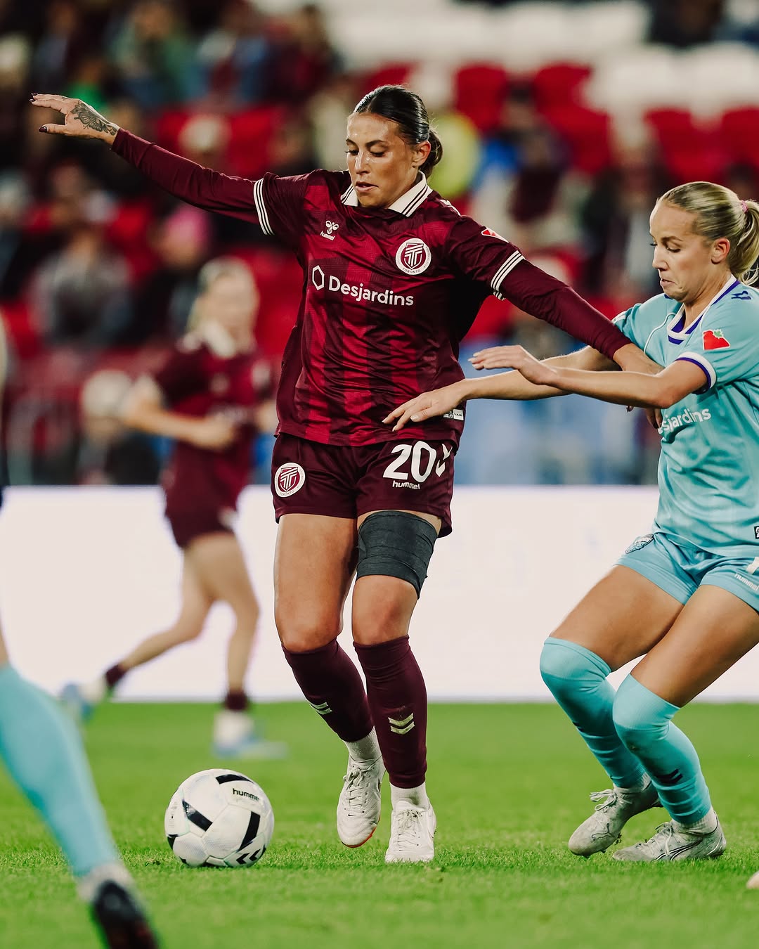 An AFC Toronto player in a maroon kit shields the ball from a Halifax Tides FC player in light blue during a Northern Super League match at BMO Field