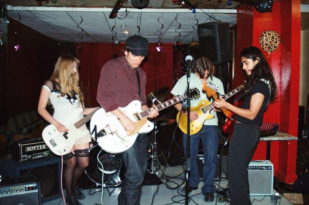 Brooklyn band Sledding performing live, four members playing bass and guitars in a small red-walled venue (photo: Katrina Stewart)