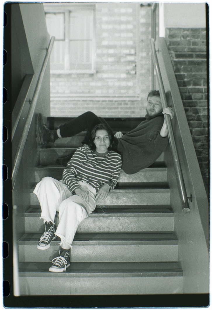 Weather Happy, UK duo Holly Carter and Harry Carter, sitting and reclining on an indoor staircase in a black-and-white photo by Alex Jackson