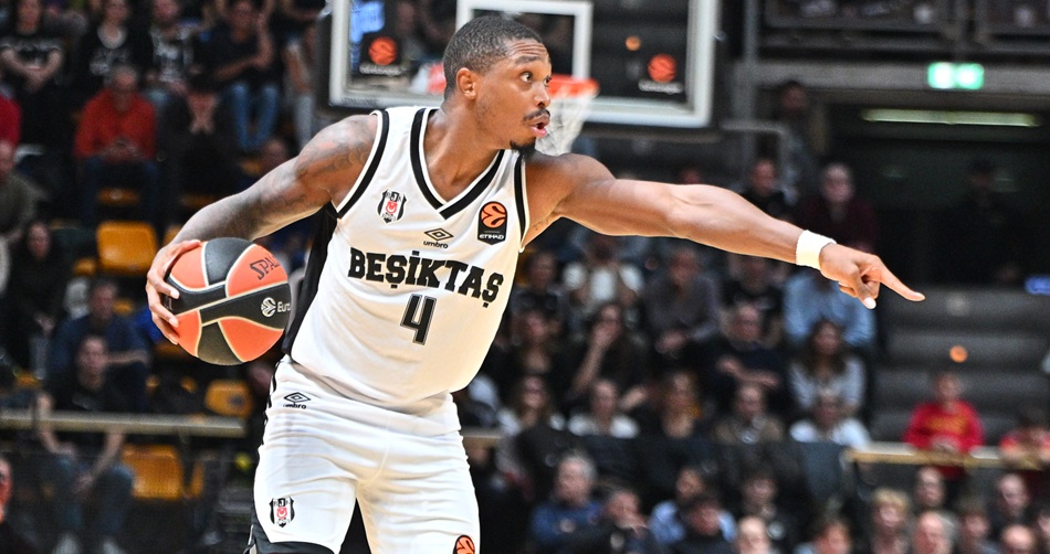 Lonnie Walker, number 4, in a white Besiktas Istanbul jersey dribbling the ball and pointing during the EuroLeague game at Virtus Bologna