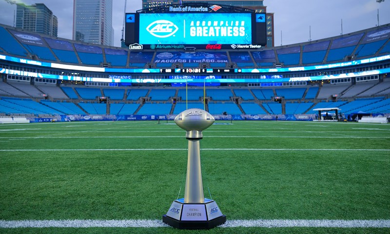 The ACC Football Championship trophy on the field at Bank of America Stadium in Charlotte, with the stadium video board reading Accomplish Greatness.