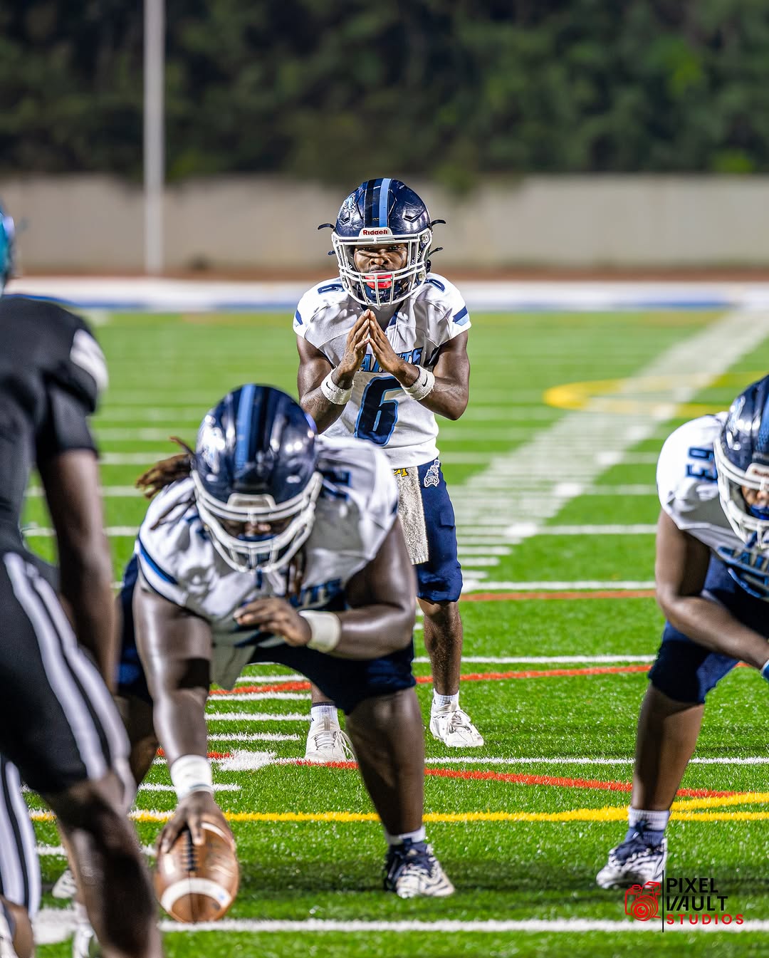 The Cedar Grove Saints offense lines up under the lights, with the quarterback wearing No. 6 clapping for the snap behind his center