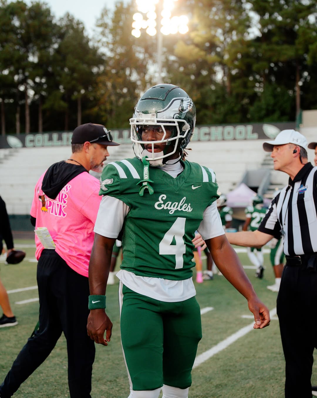 A Collins Hill Eagles player wearing green jersey No. 4 and his helmet walks on the field at Collins Hill as a coach and a game official stand nearby