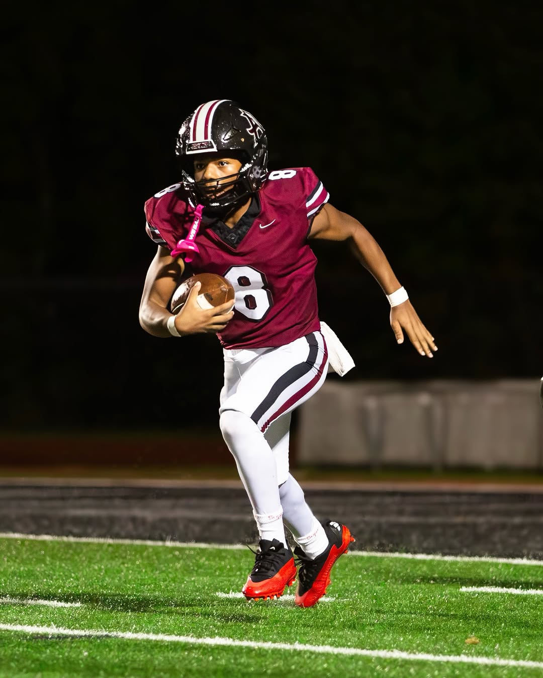 An Alpharetta Raiders ball carrier in a maroon jersey with No. 8 runs with the football under the lights during a night game
