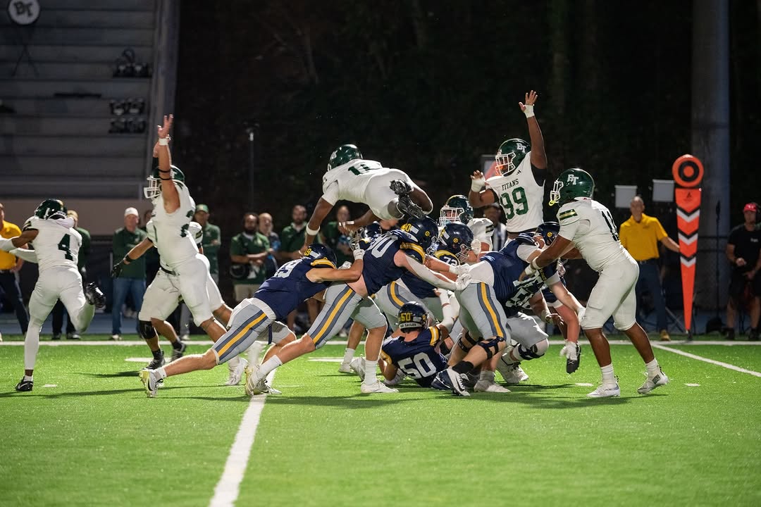 Marist War Eagles players in navy jerseys surge off the line to pressure a field goal attempt during the Homecoming night game under the lights