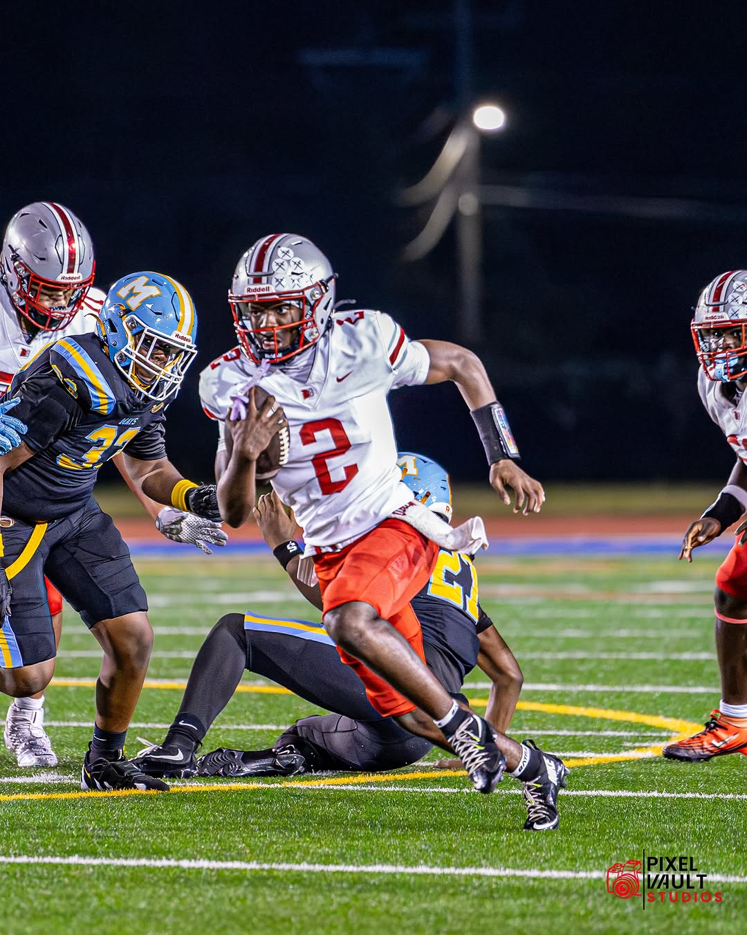 Banneker Trojans quarterback No. 2 in a white jersey and red pants breaks away with the football as defenders close in during a night game