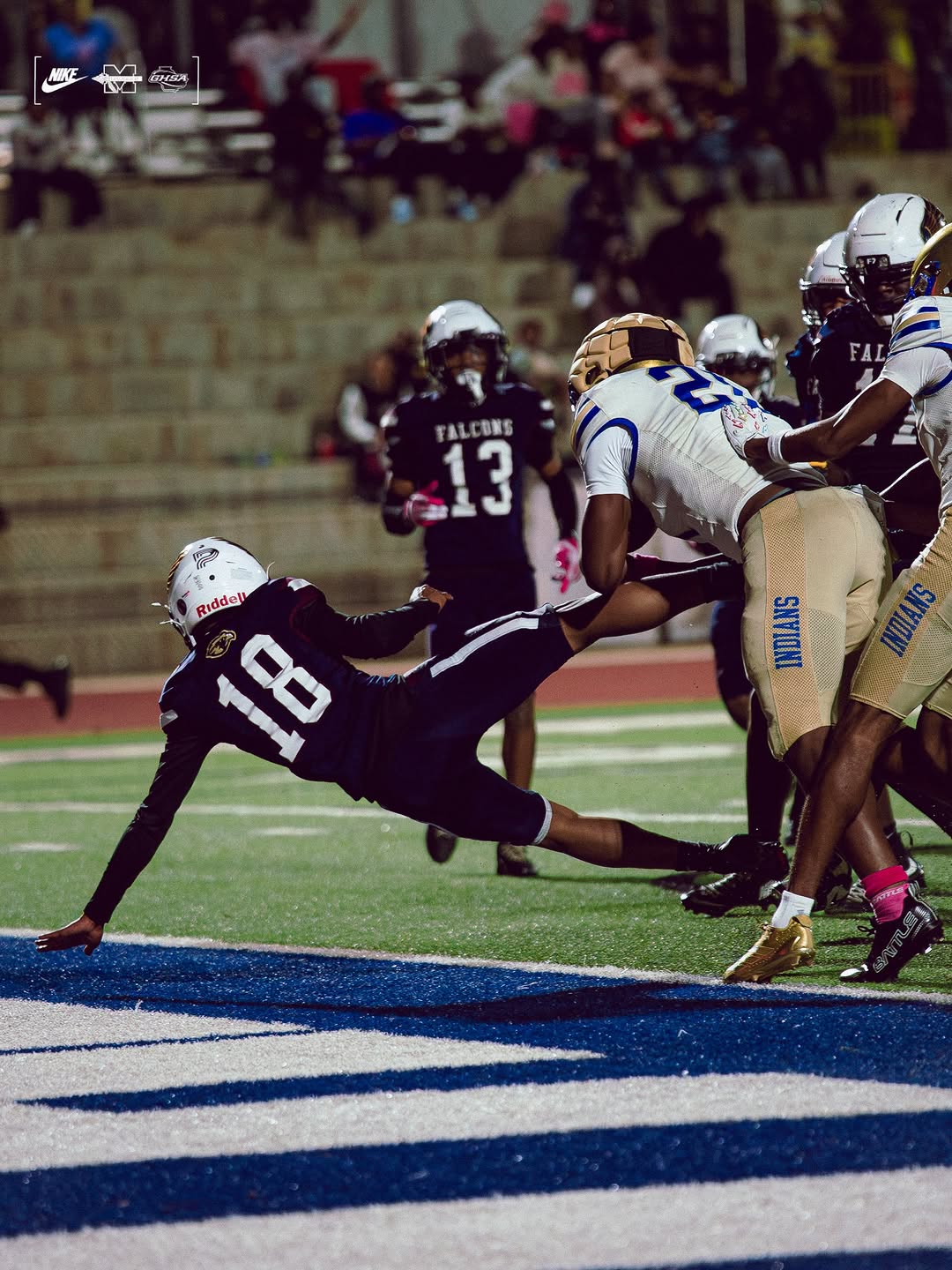 A McEachern ball carrier in a white jersey and gold Indians pants is tackled at the goal line by a defender during night game action
