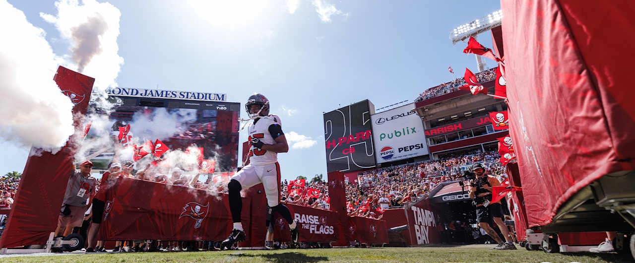 A Tampa Bay Buccaneers player runs onto the field at Raymond James Stadium through smoke and flags.