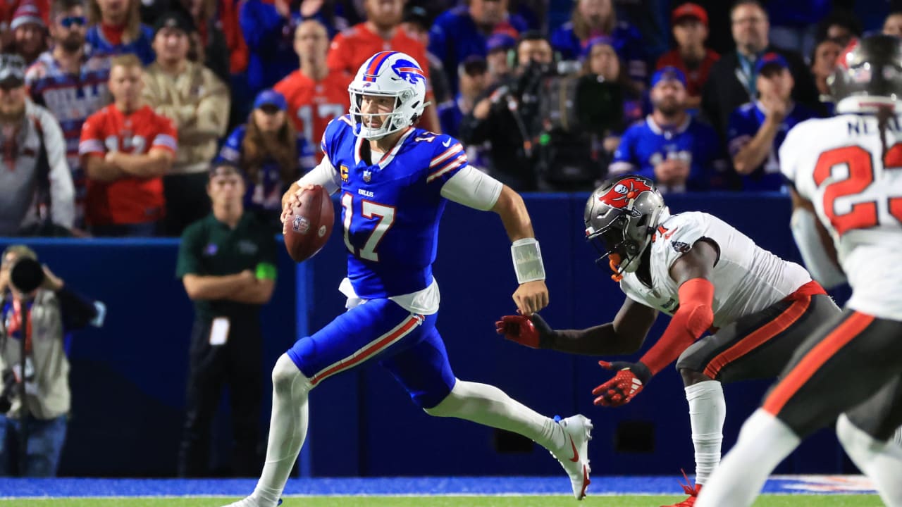 Buffalo Bills quarterback Josh Allen scrambles with the ball as defenders close in.
