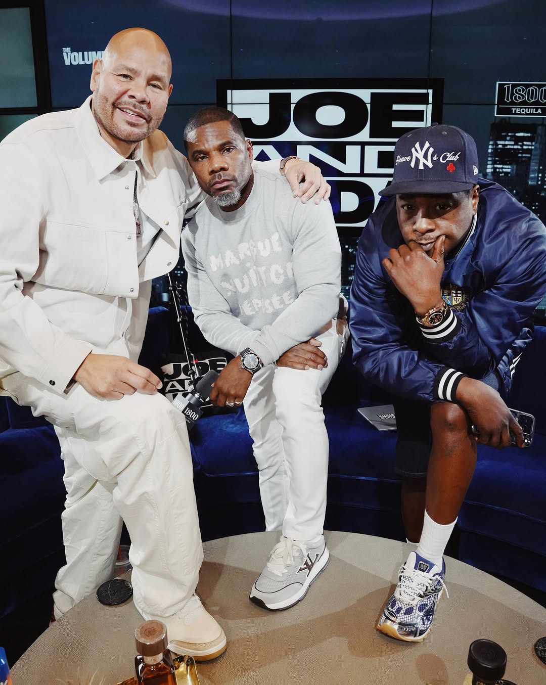 Kirk Franklin sits between Fat Joe and Jadakiss on a podcast set, wearing a gray sweatshirt and white pants.