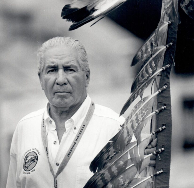 Oren Lyons in an Iroquois Nationals shirt holding a feather staff