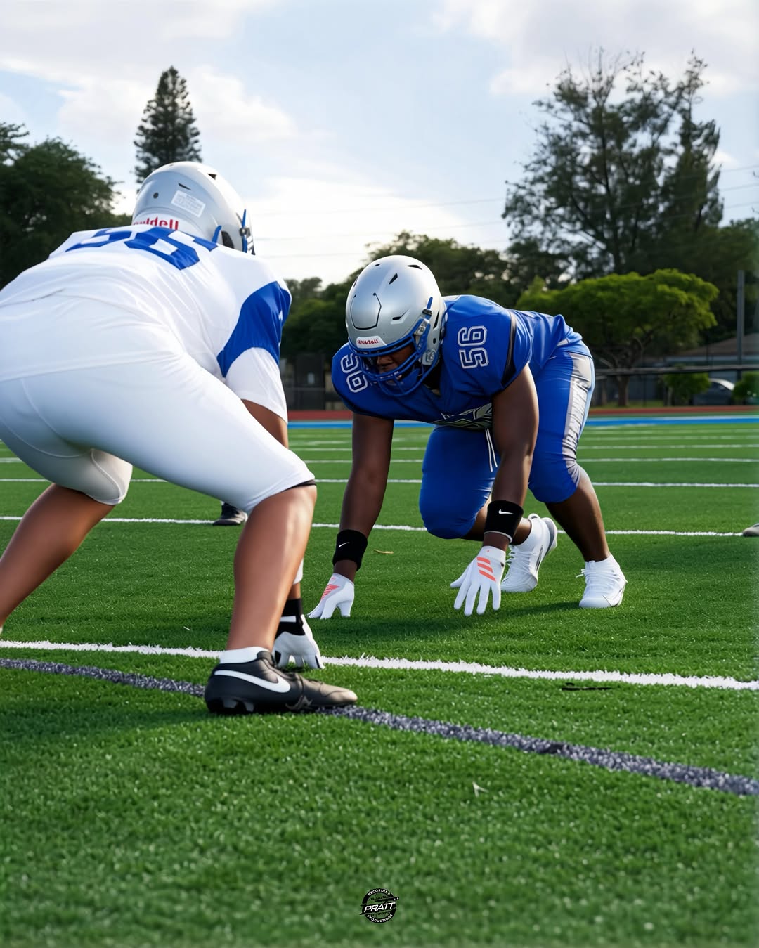 Two Dillard Panthers linemen, one in blue and one in white, face off in three-point stances on the practice field