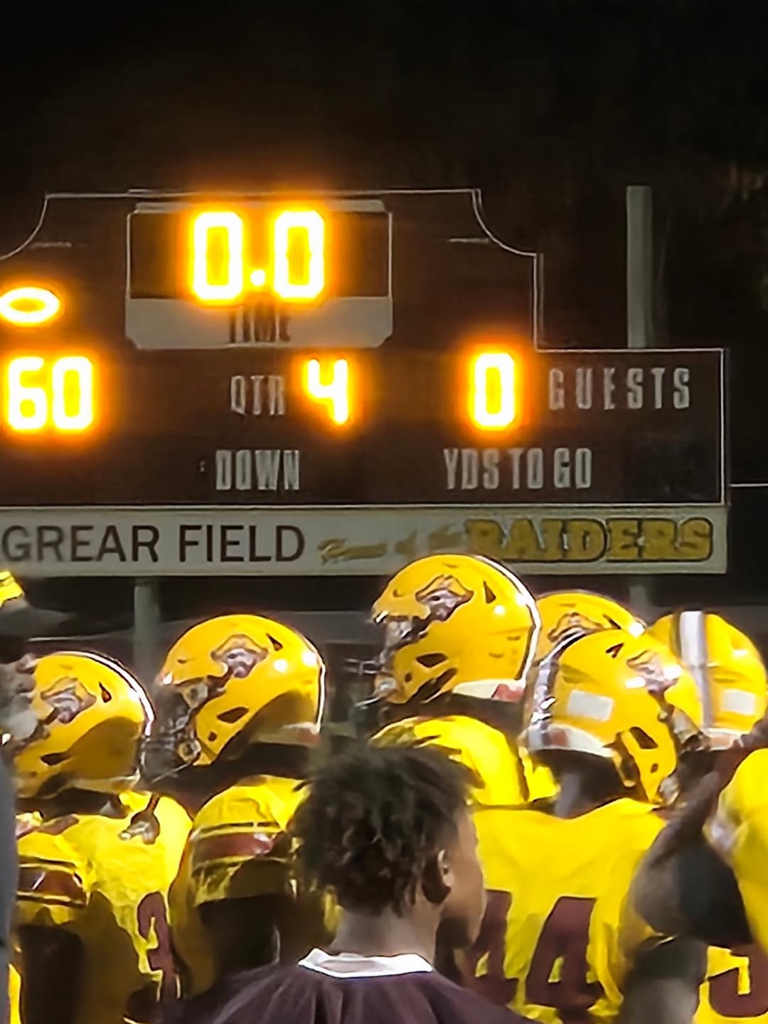 Glades Central Raiders players in gold helmets and jerseys celebrate on the field in front of the Effie Grear Field scoreboard after a win